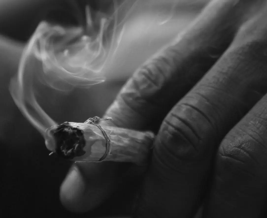Smoke curling from a hand-rolled cigarette, in black and white