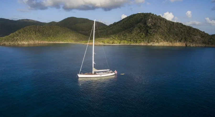 A lone yacht anchored beneath green hills